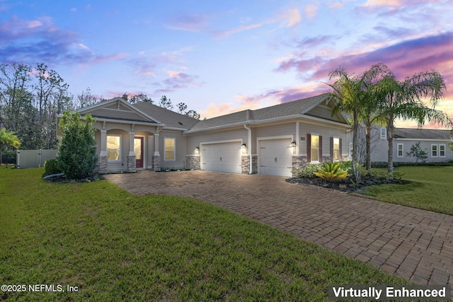 view of front of property featuring decorative driveway, a lawn, an attached garage, fence, and stone siding