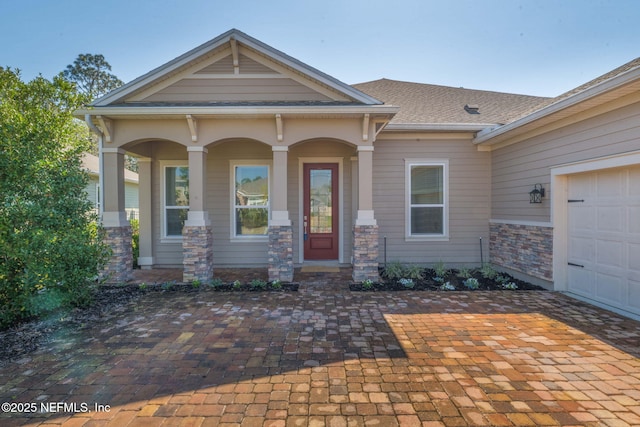 view of front of house featuring stone siding, covered porch, roof with shingles, and an attached garage