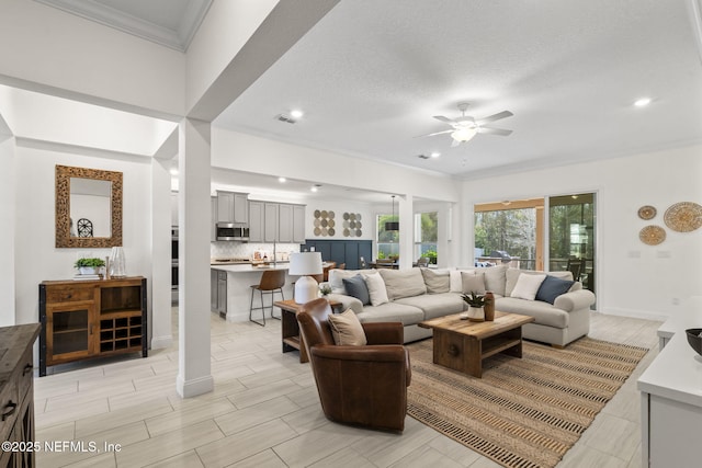 living room featuring wood finish floors, a ceiling fan, baseboards, visible vents, and crown molding