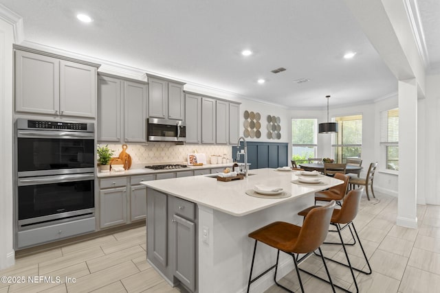 kitchen with tasteful backsplash, appliances with stainless steel finishes, ornamental molding, gray cabinets, and a sink