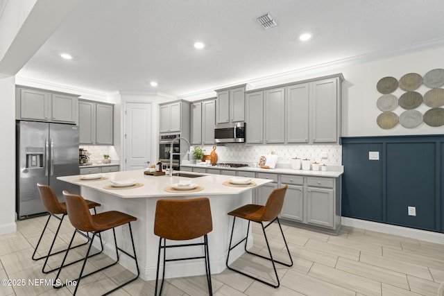 kitchen with stainless steel appliances, gray cabinets, visible vents, and a kitchen breakfast bar