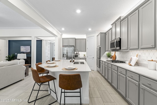 kitchen with a kitchen bar, stainless steel appliances, a sink, and gray cabinetry