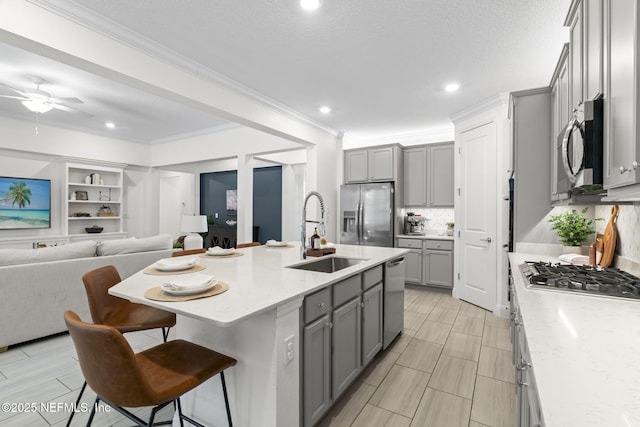 kitchen featuring appliances with stainless steel finishes, a breakfast bar area, a sink, and gray cabinetry