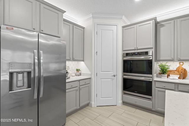 kitchen with gray cabinets, backsplash, appliances with stainless steel finishes, ornamental molding, and a textured ceiling