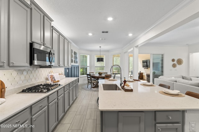 kitchen featuring gray cabinetry, appliances with stainless steel finishes, open floor plan, a sink, and an island with sink