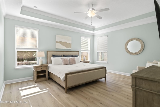 bedroom with baseboards, a raised ceiling, light wood-style flooring, and crown molding