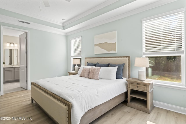 bedroom featuring light wood finished floors, multiple windows, a tray ceiling, and crown molding