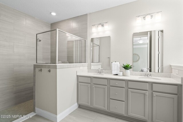 full bathroom with a textured ceiling, double vanity, walk in shower, and a sink