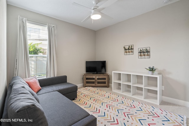 living area with a ceiling fan, light colored carpet, and baseboards