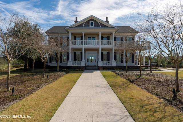 greek revival inspired property with covered porch, a chimney, a front yard, and a balcony