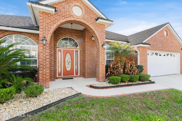 entrance to property with a garage, concrete driveway, a shingled roof, and brick siding