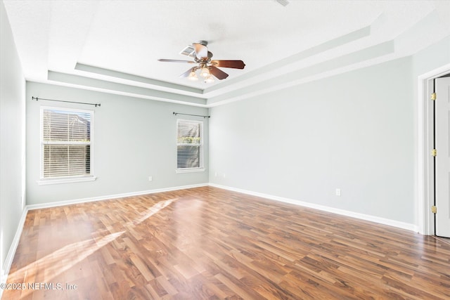 empty room with a raised ceiling, baseboards, and wood finished floors