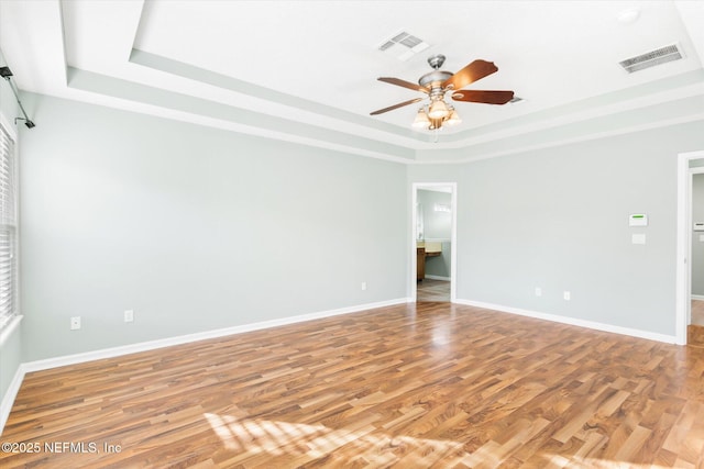 empty room featuring a raised ceiling, visible vents, baseboards, and wood finished floors