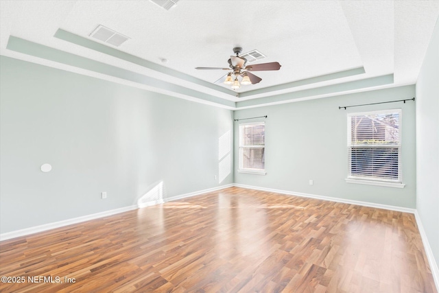 empty room with a wealth of natural light, a tray ceiling, visible vents, and wood finished floors