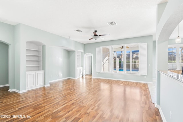 unfurnished living room with light wood-type flooring, visible vents, arched walkways, and built in features