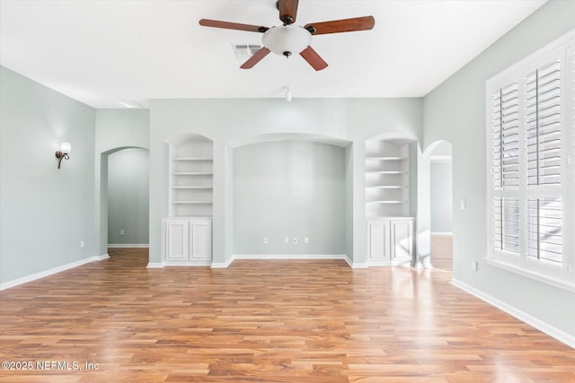 unfurnished room featuring visible vents, built in features, arched walkways, and baseboards