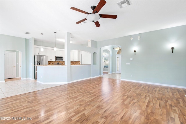 unfurnished living room with arched walkways, a ceiling fan, visible vents, and light wood-style floors