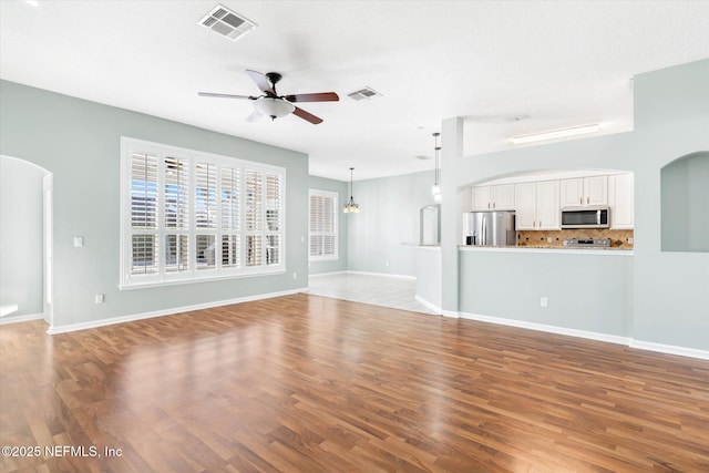 unfurnished living room featuring visible vents, arched walkways, ceiling fan, and wood finished floors