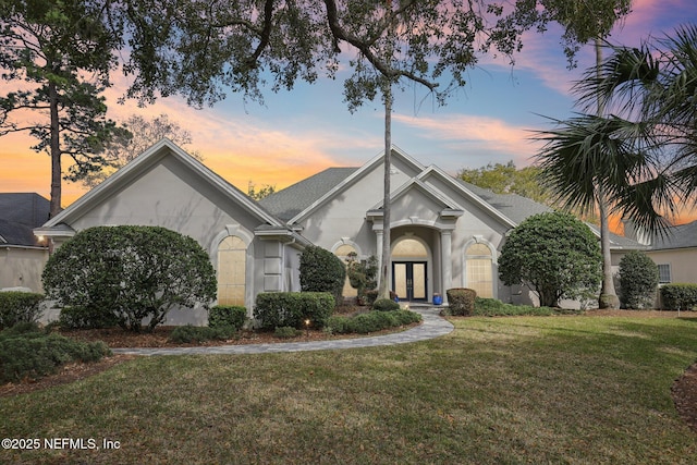 view of front of home with a shingled roof, french doors, a yard, and stucco siding