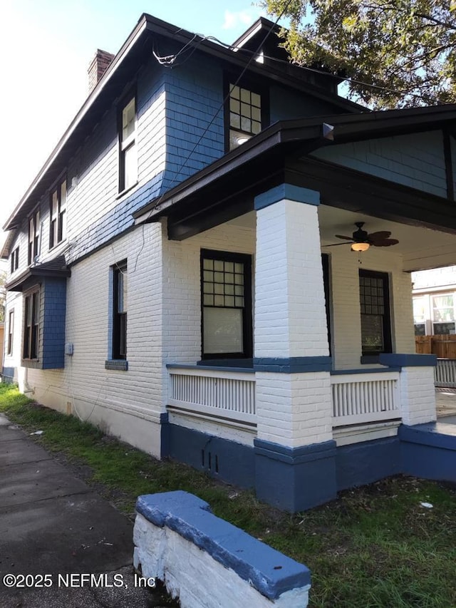 view of property exterior featuring covered porch, brick siding, ceiling fan, and a chimney