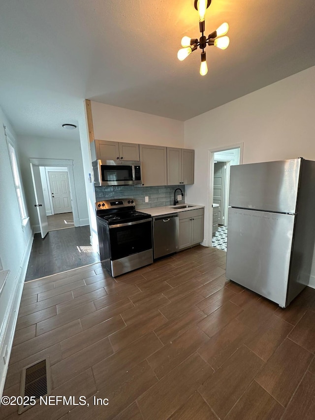 kitchen featuring light countertops, backsplash, gray cabinetry, appliances with stainless steel finishes, and wood tiled floor