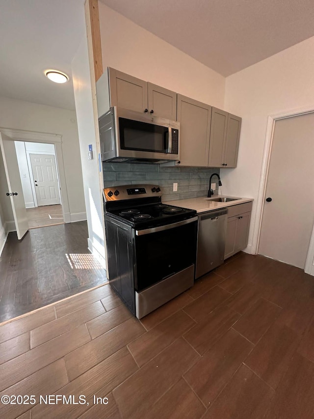 kitchen with tasteful backsplash, gray cabinets, stainless steel appliances, light countertops, and a sink