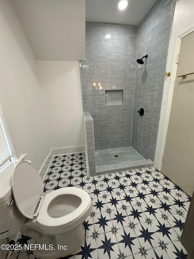 bathroom with a tile shower, toilet, and baseboards