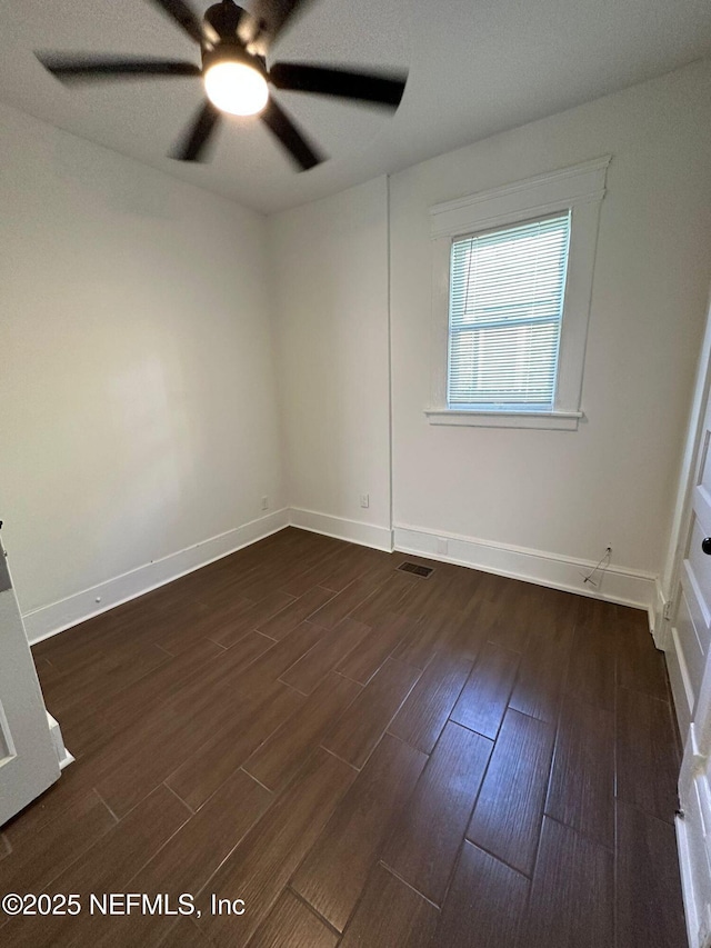 spare room featuring dark wood-style flooring, visible vents, ceiling fan, and baseboards