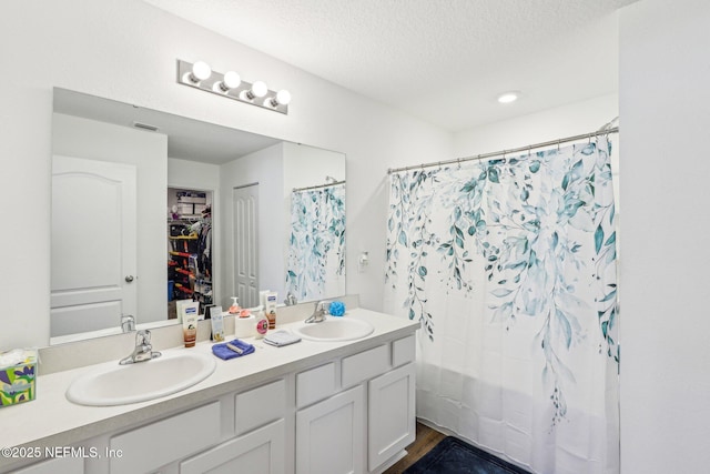 bathroom featuring a walk in closet, a sink, a textured ceiling, and double vanity