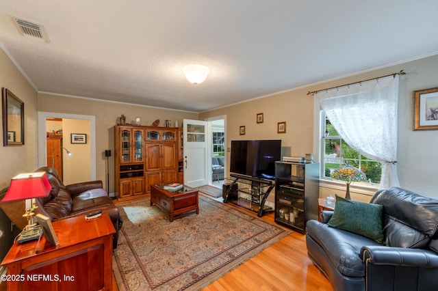 living room with a textured ceiling, light wood-style flooring, visible vents, and crown molding