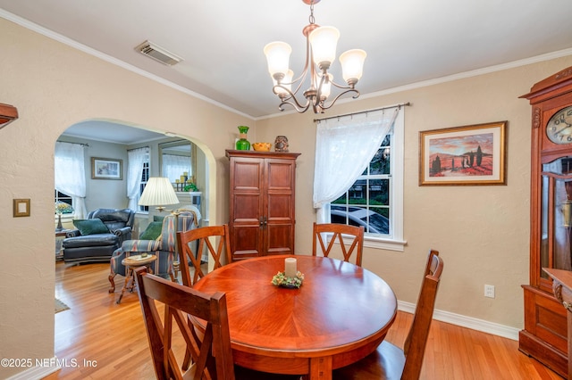 dining room featuring arched walkways, visible vents, baseboards, ornamental molding, and light wood-type flooring