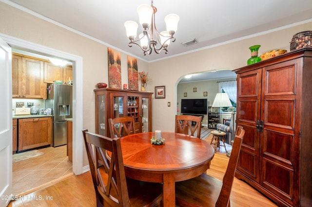 dining space with visible vents, arched walkways, ornamental molding, an inviting chandelier, and light wood-style floors