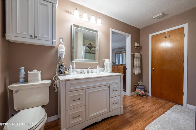 bathroom featuring visible vents, toilet, wood finished floors, walk in shower, and vanity