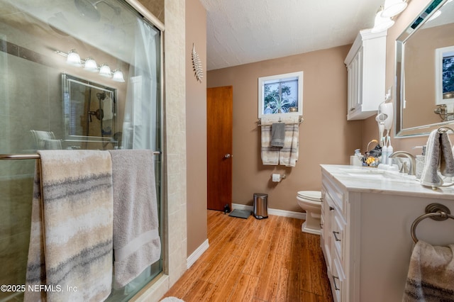 full bath featuring a stall shower, baseboards, toilet, wood finished floors, and vanity