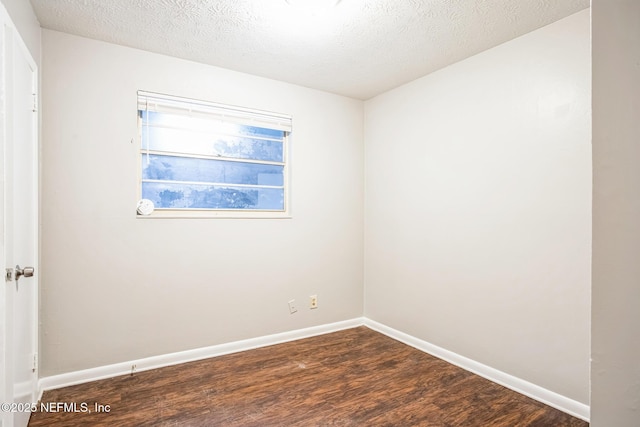 spare room with dark wood-style floors, a textured ceiling, and baseboards