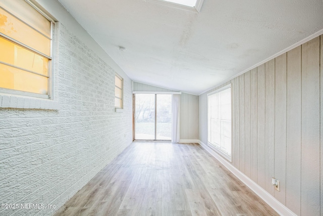 spare room featuring wooden walls, baseboards, vaulted ceiling, and wood finished floors