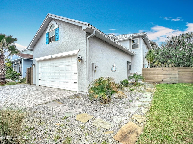 view of property exterior featuring decorative driveway, an attached garage, fence, and stucco siding