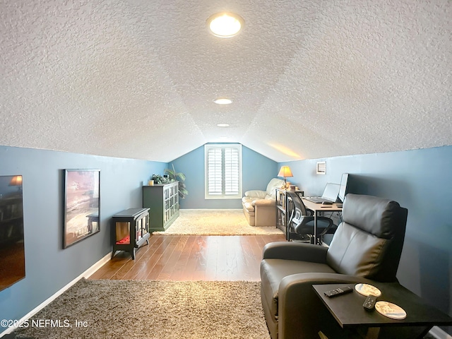 interior space with vaulted ceiling, a textured ceiling, baseboards, and wood finished floors