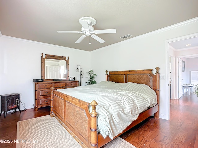 bedroom with a wood stove, dark wood-style floors, visible vents, and ornamental molding