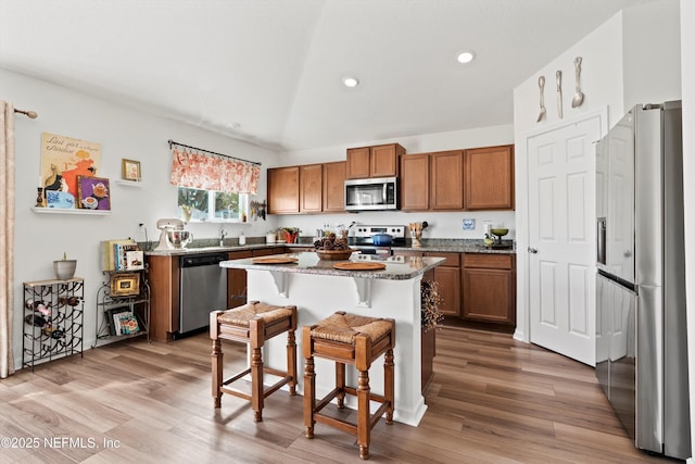 kitchen featuring a center island, a kitchen breakfast bar, appliances with stainless steel finishes, brown cabinets, and dark stone counters