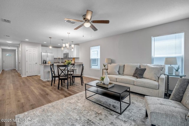 living room featuring a textured ceiling, light wood finished floors, visible vents, and baseboards