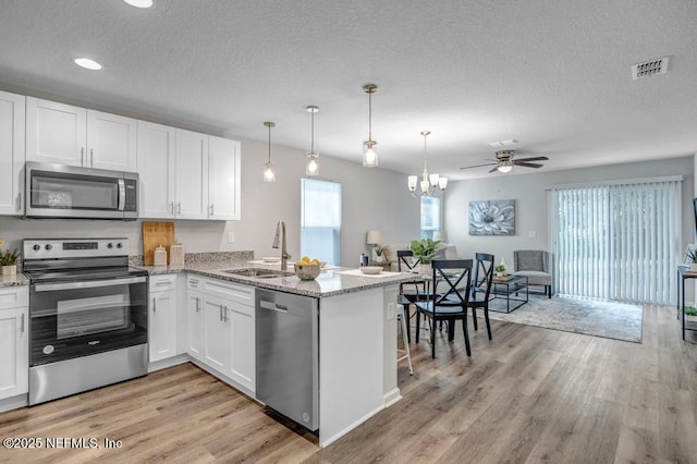 kitchen with a peninsula, appliances with stainless steel finishes, visible vents, and white cabinets