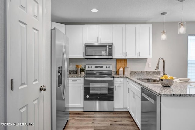 kitchen featuring appliances with stainless steel finishes, pendant lighting, white cabinets, and a peninsula