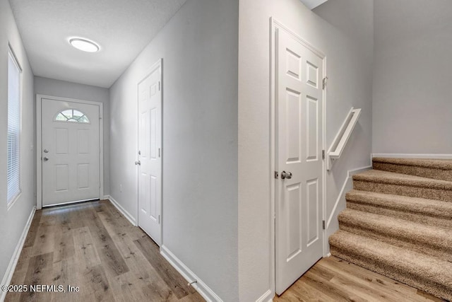 entryway with light wood-style flooring, baseboards, and stairs