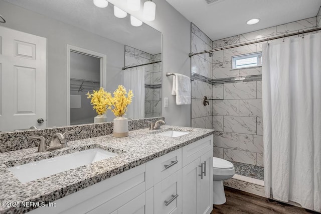 bathroom featuring double vanity, a shower stall, a sink, and wood finished floors