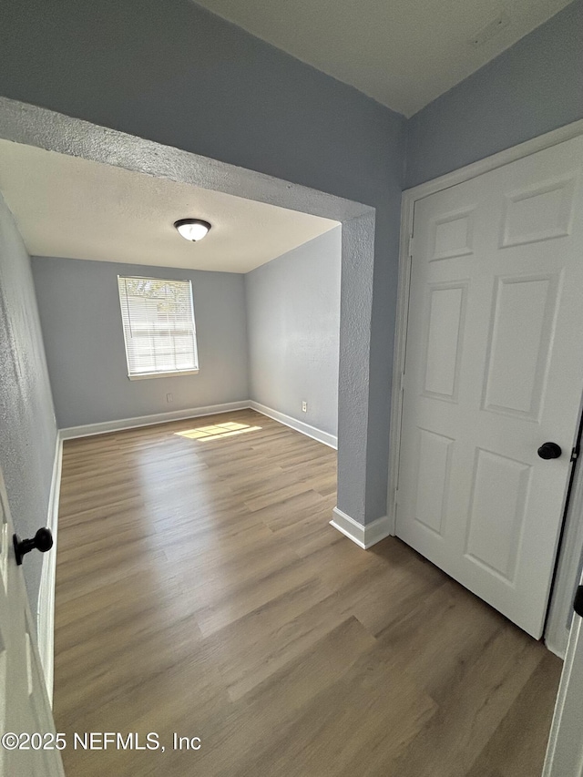 unfurnished bedroom featuring light wood-style floors, baseboards, and a textured ceiling