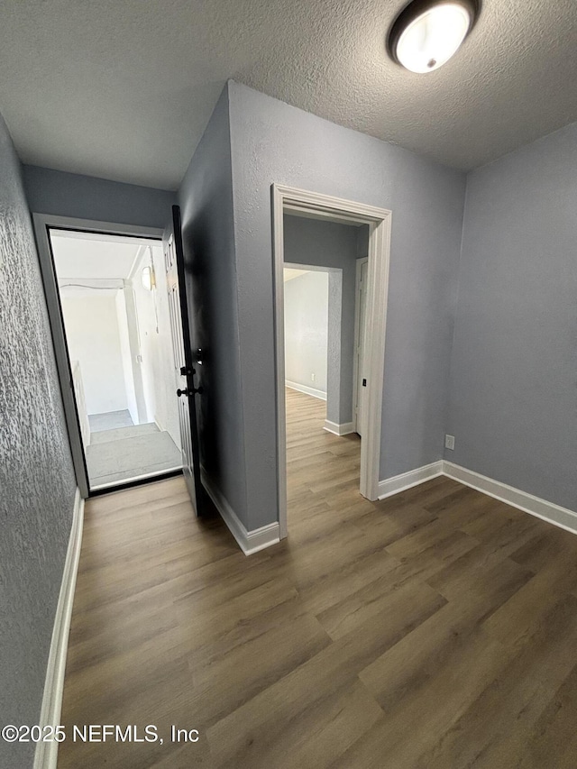 corridor with a textured ceiling, a textured wall, wood finished floors, and baseboards