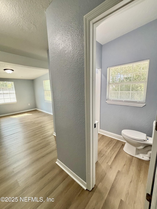 bathroom with baseboards, a textured wall, toilet, wood finished floors, and a textured ceiling