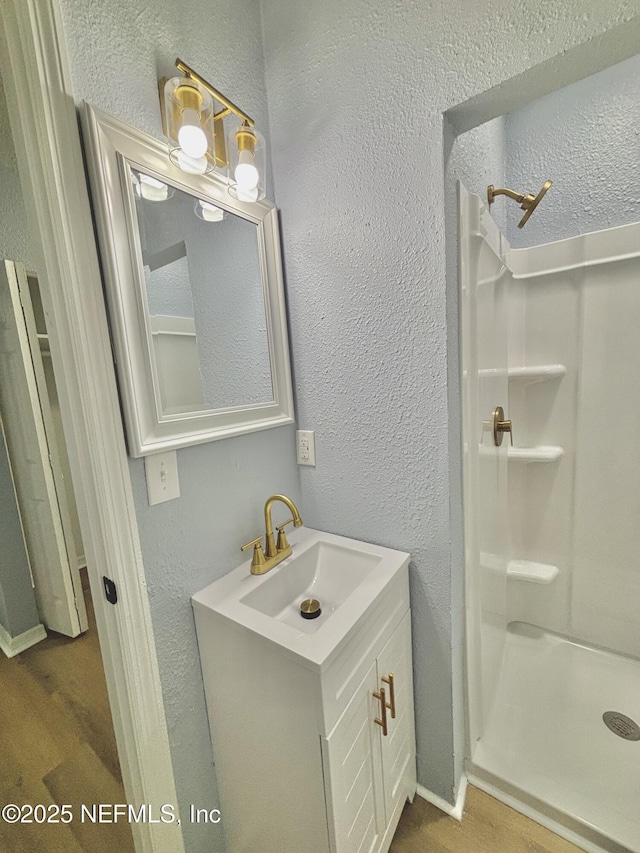 bathroom featuring a stall shower, vanity, and a textured wall