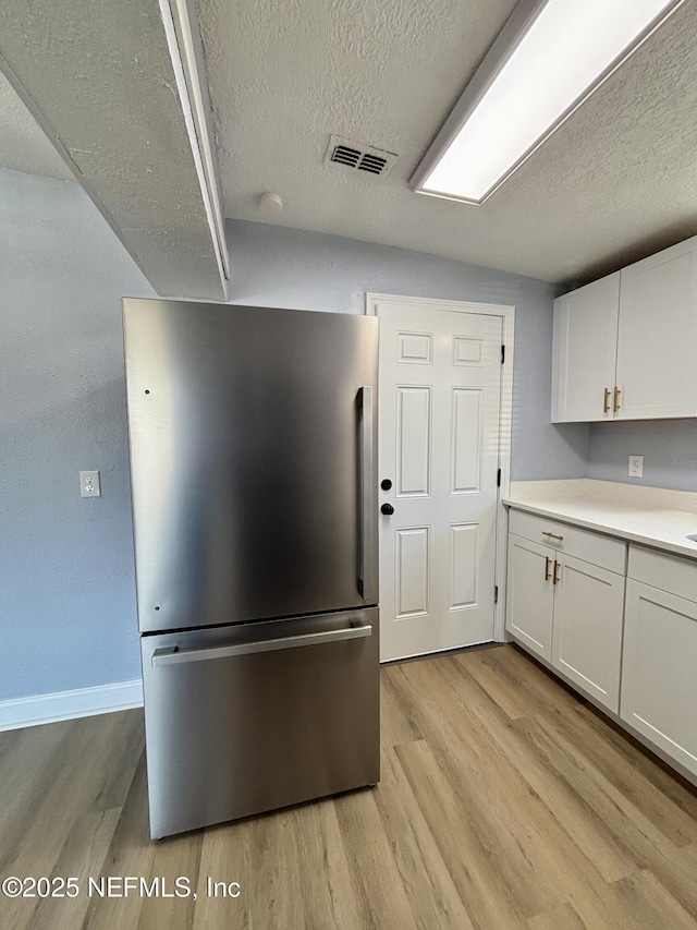 kitchen with visible vents, light countertops, freestanding refrigerator, and white cabinets